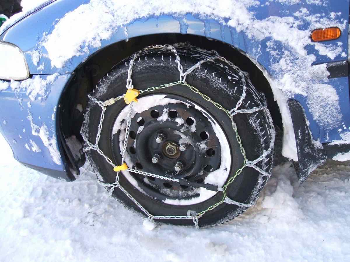 Snow chains fitted on the front tire of a car in snow